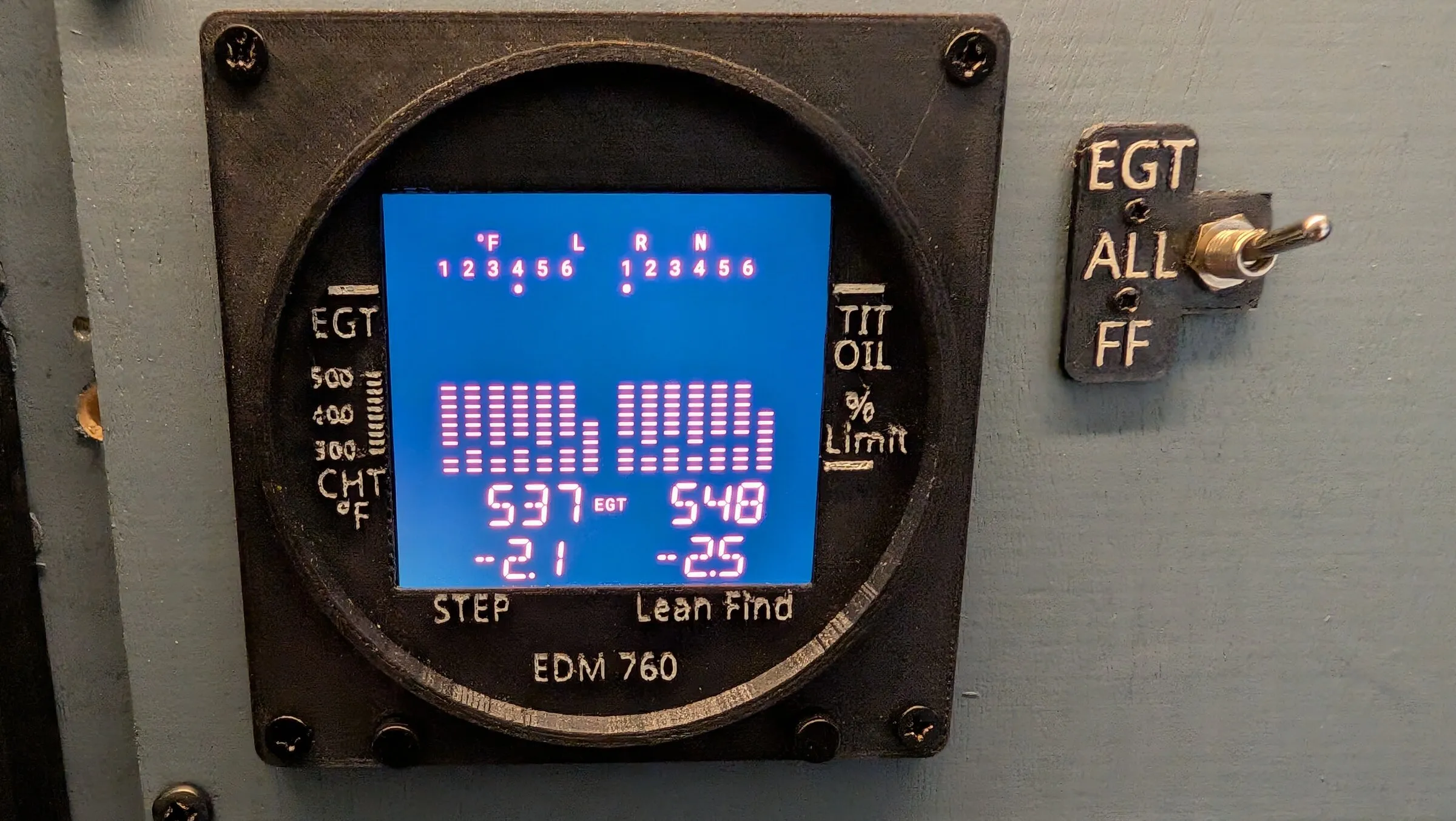 The round engine monitor replica showing exhaust temperature bars for both engines, next to its mode toggle switch